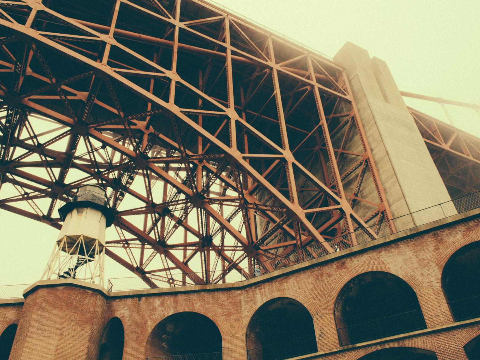 Unterseite einer rostfarbenen Stahlbr&uuml;cke mit Backsteinbogen aus der Froschperspektive
