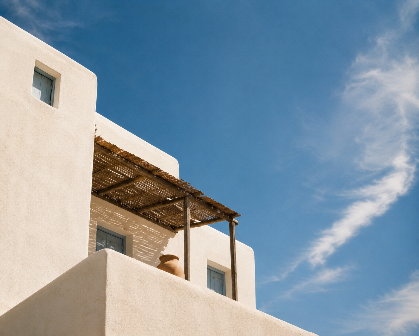 Wei&szlig;es griechisches Ferienhaus mit Holzdach vor blauem Sommerhimmel