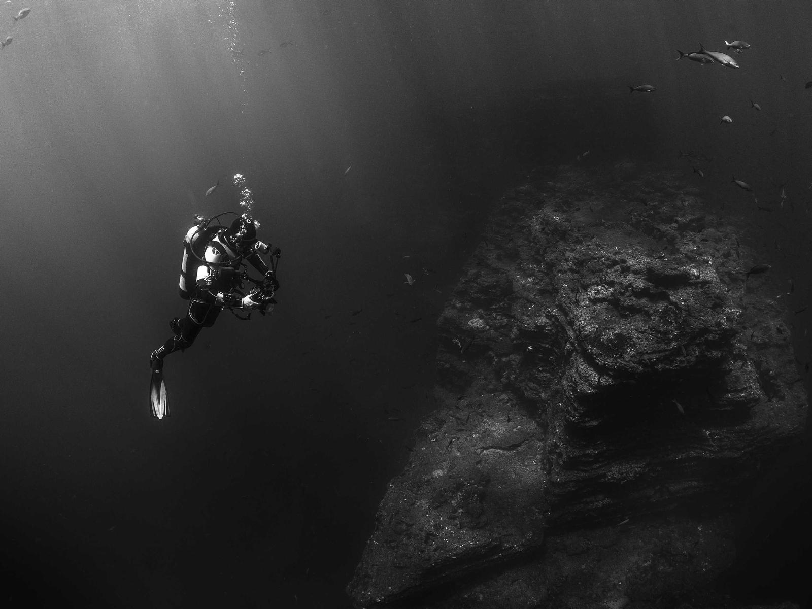 Taucher schwebt in schwarzwei&szlig;er Unterwasseraufnahme neben Felsformation