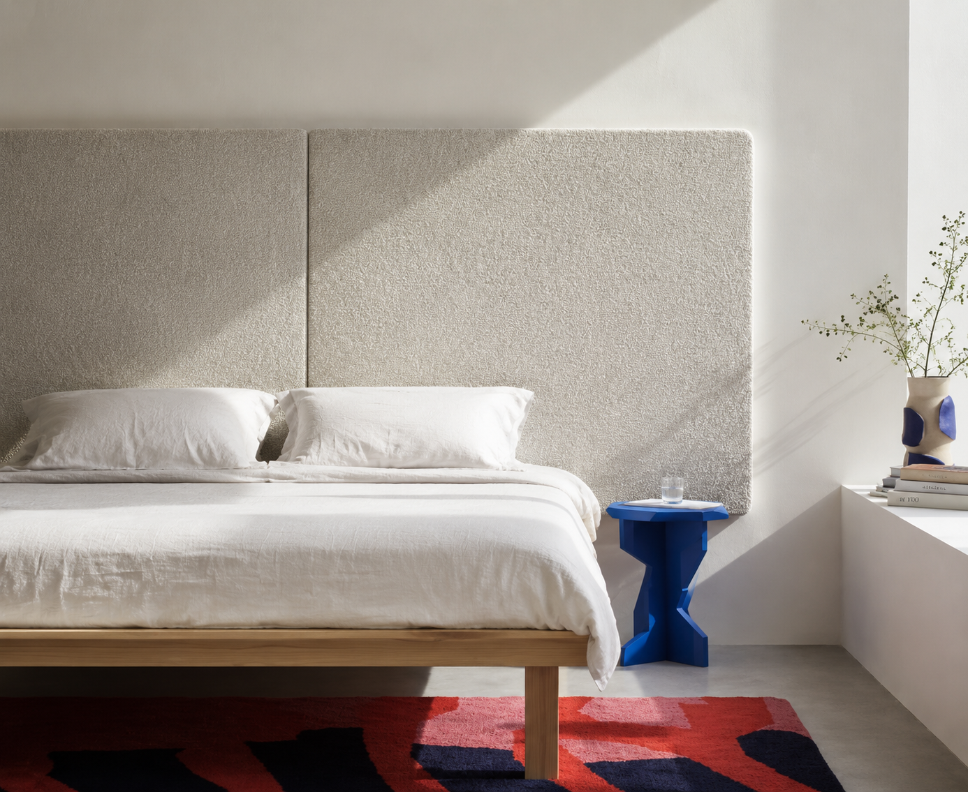 Helles Schlafzimmer einer Ferienwohnung mit wei&szlig;em Bett und blauem Beistelltisch